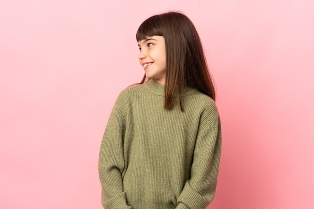 Menina isolada em um fundo rosa olhando para o lado e sorrindo