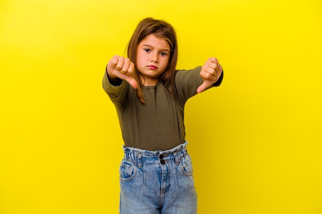 Foto menina isolada na parede amarela mostrando o polegar para baixo