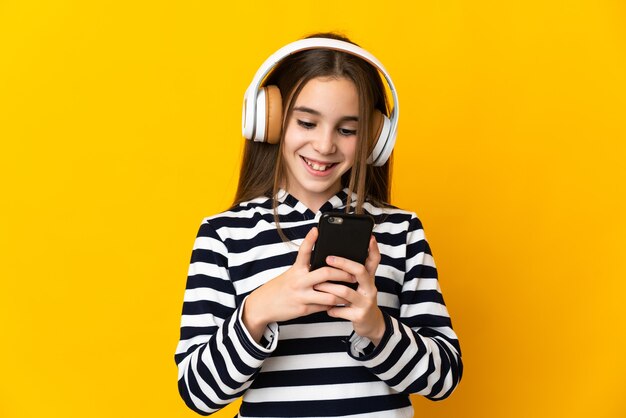 Menina isolada na parede amarela ouvindo música e olhando para o celular