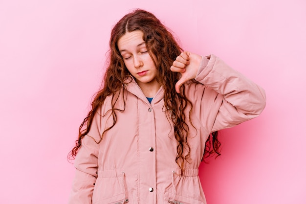 Menina isolada na parede rosa, mostrando um gesto de antipatia, polegares para baixo. Conceito de desacordo