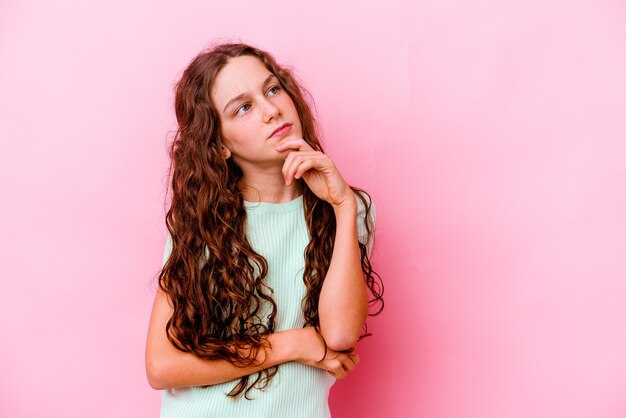 Menina isolada na parede rosa pensando e olhando para cima, sendo reflexiva, contemplando, tendo uma fantasia