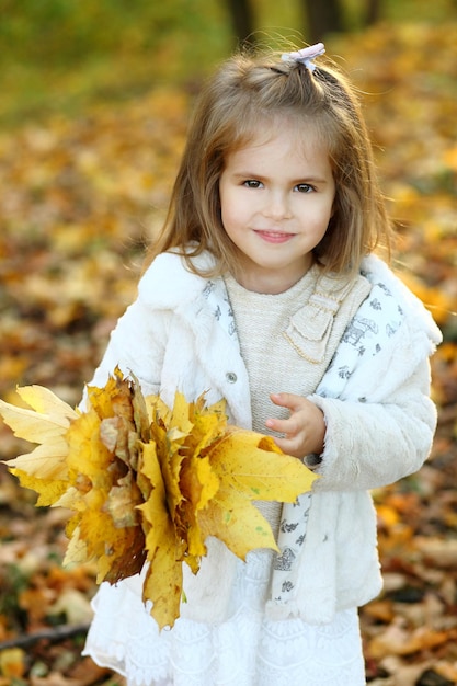 Menina joga folhas de outono no parque de outono