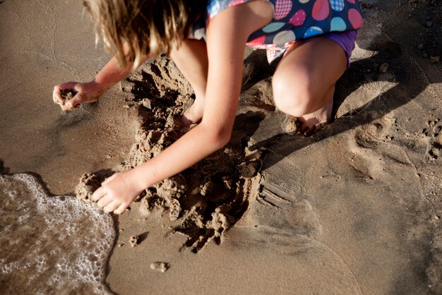 Menina jogando areia à beira-mar