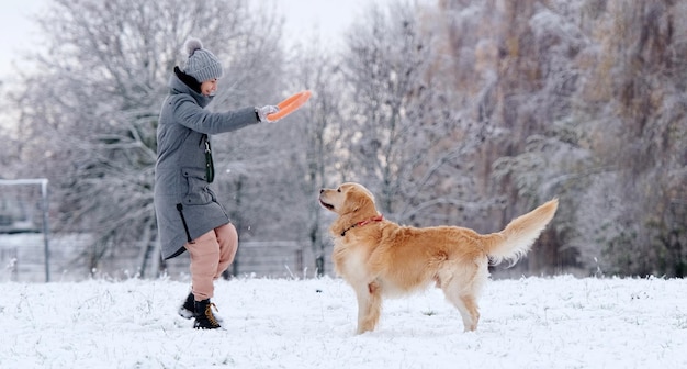 Menina jogando brinquedo de anel para o adorável cão golden retriever em um campo de neve no inverno