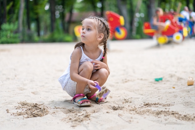 Menina jogando caixa de areia Playground cavar areia pá construção figura de areia dia de verão. Criança Caucasiana Feminino 5 anos Divirta-se ao ar livre