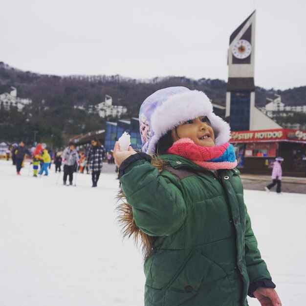 Foto menina jogando neve enquanto está de pé no campo contra o céu