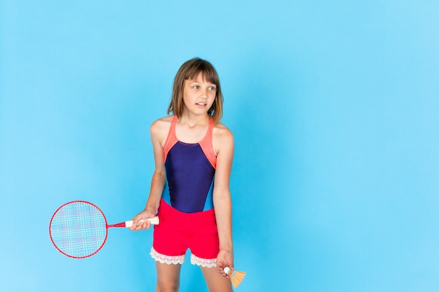 Menina jovem adolescente pulando e jogando badminton na parede azul