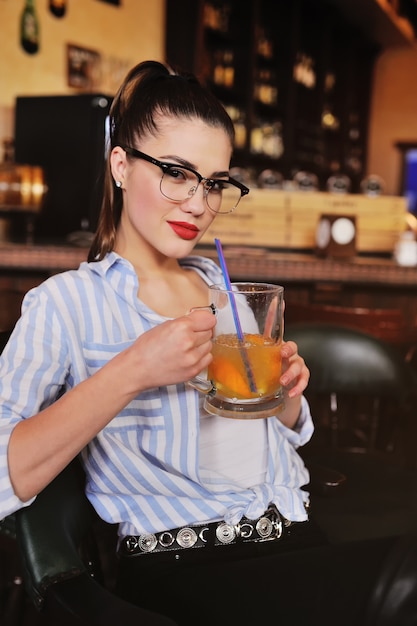 Menina jovem, com, óculos, é, segurando, um, assalte cerveja, ou, um, cerveja, laranja, coquetel, frente, um bar, ou, um, bar