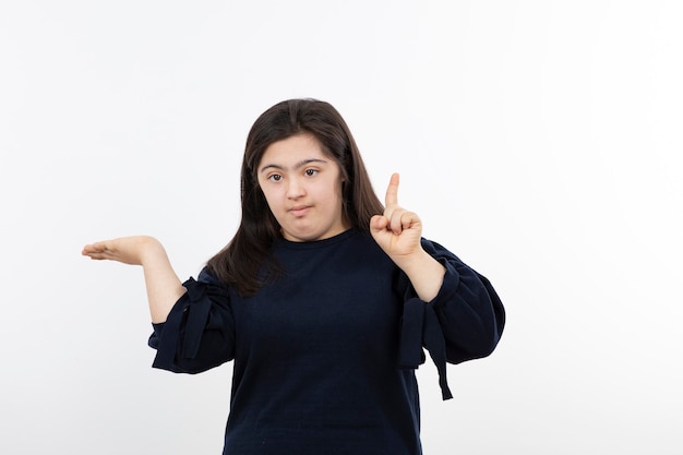 Menina jovem com síndrome de down no suéter preto em pé sobre o branco.