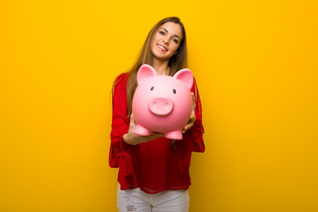 Menina jovem, com, vestido vermelho, sobre, parede amarela, segurando, um, piggybank