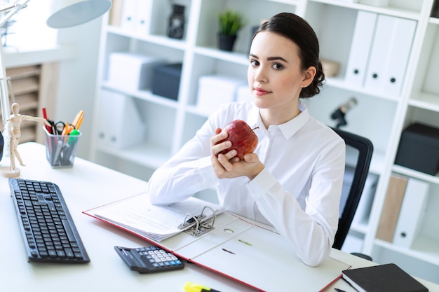 Menina jovem, em, escritório, trabalhando, com, documentos, e, segurando uma maçã