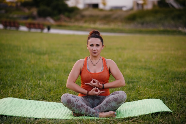 Menina jovem fazendo ioga ao ar livre, no parque durante o pôr do sol. Estilo de vida saudável