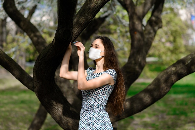 Menina, jovem mulher com uma máscara médica protetora estéril no rosto no jardim de primavera