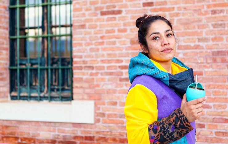 Foto menina latina olhando para a câmera em roupas coloridas e bebendo mate