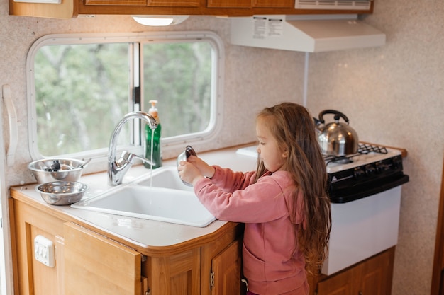 Menina lavando pratos na cozinha de um trailer de viagem