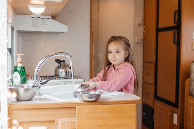 Menina lavando pratos na cozinha de um trailer de viagem