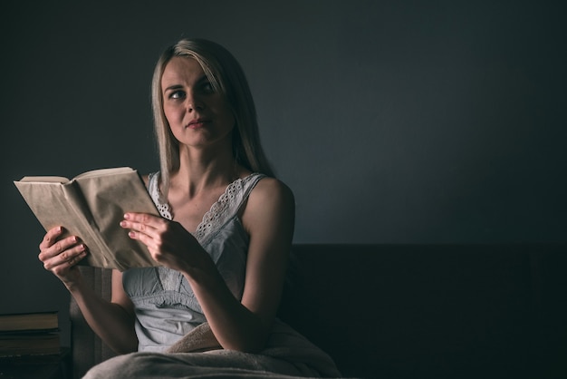 Menina lendo com entusiasmo um livro best-seller debaixo de um tapete em um sofá confortável com uma lâmpada