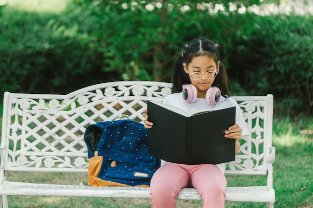 Menina lendo um livro sentada em um banco no parque