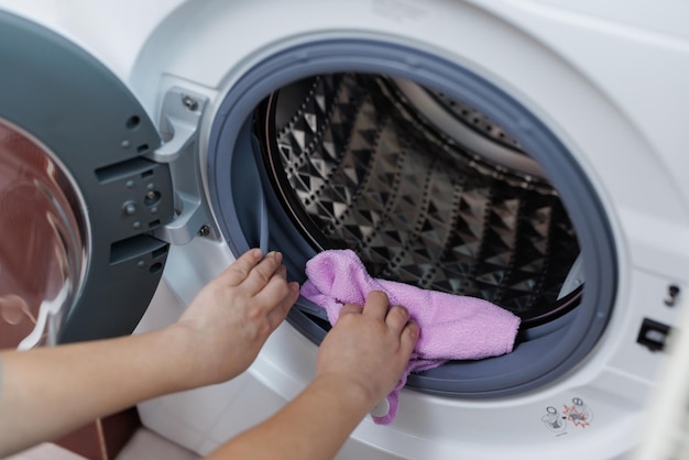 Menina limpa a porta da máquina de lavar a seco com um guardanapo rosa A dona de casa está envolvida na limpeza úmida