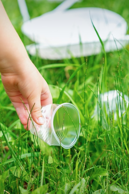 Menina limpa utensílios de plástico na grama verde do parque