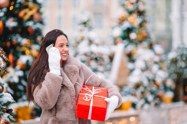 Menina linda com presente vermelho no Natal com smartphone na neve ao ar livre