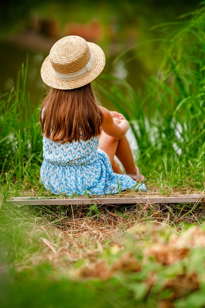 Menina linda com um chapéu e um vestido na margem de um lago fabuloso