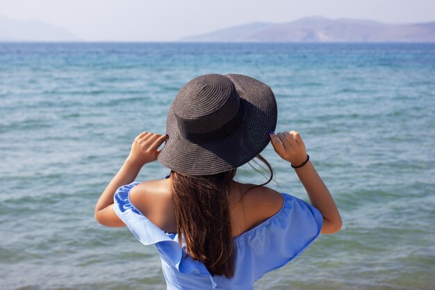 Menina linda com um chapéu olhando para o mar