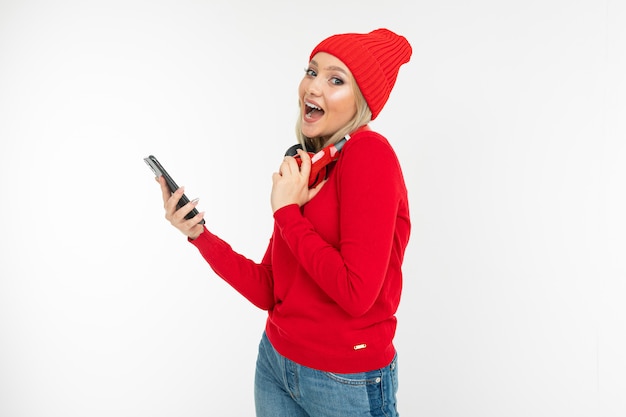 Menina linda com um telefone nas mãos e fones de ouvido vermelhos no pescoço em um fundo branco com espaço de cópia