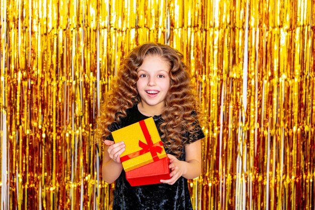 Menina linda criança alegre e fofa em um fundo dourado de férias com uma caixa de presente nas mãos