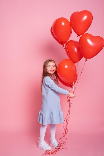 Menina linda criança com balões românticos de coração vermelho no conceito de fundo rosa do dia dos namorados