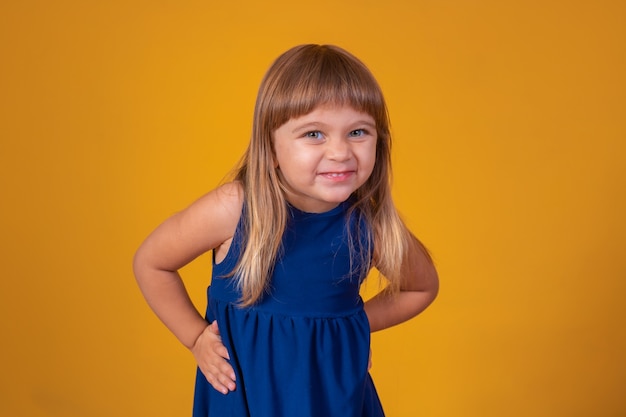 Menina linda criança loira sorrindo olhando para a câmera em fundo amarelo com espaço livre para texto.