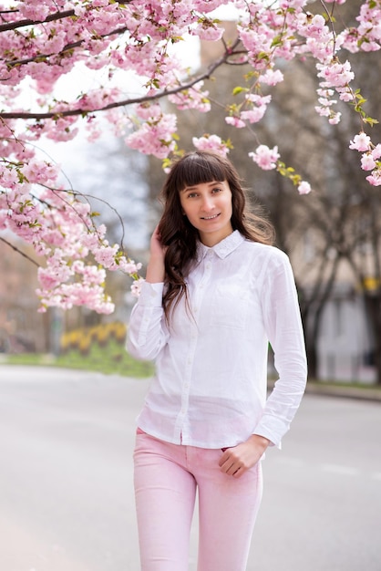 Menina linda de pé perto da flor de sakura na rua da cidade