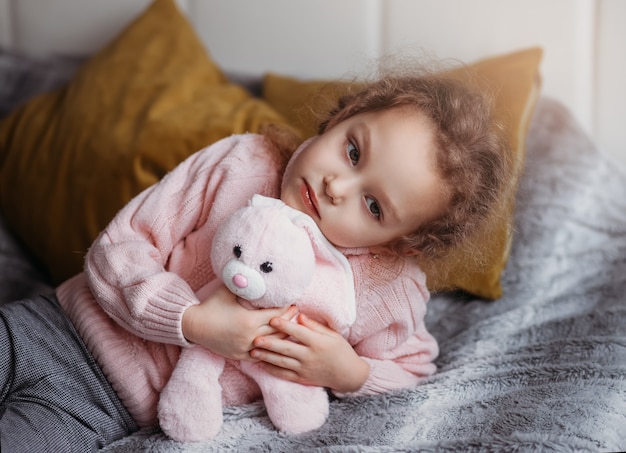 Menina linda deitada na cama com um brinquedo macio e triste