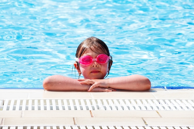 Menina linda em copos de água cor de rosa na piscina