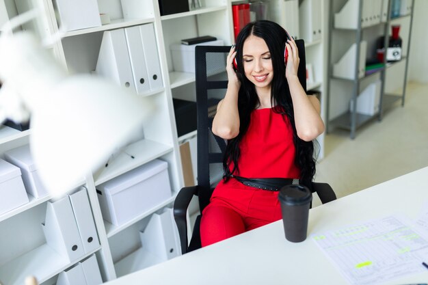 Menina linda em fones de ouvido senta-se no escritório à mesa.