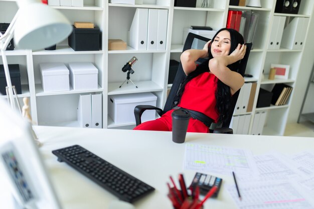 Menina linda em fones de ouvido senta-se no escritório à mesa.