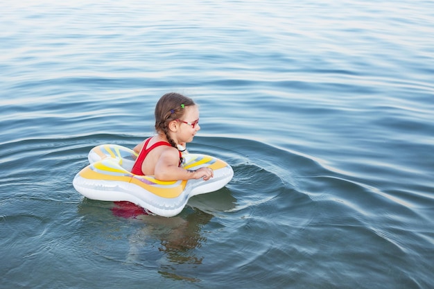 Menina linda em um maiô vermelho nada em um anel de borracha no mar