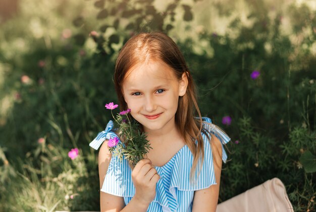 Menina linda em um vestido azul com flores na natureza no verão