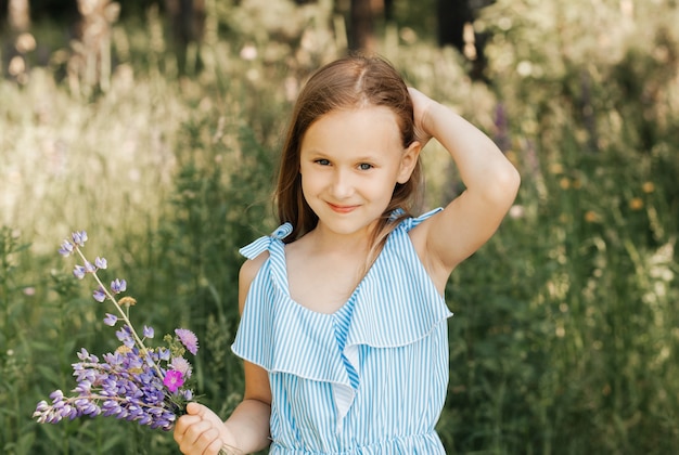 Menina linda em um vestido azul com flores na natureza no verão