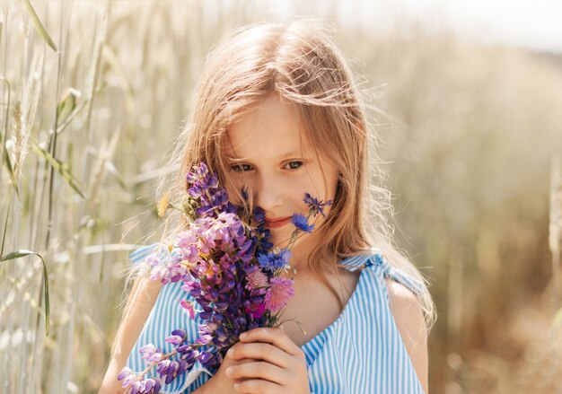 Menina linda em um vestido azul com flores na natureza no verão