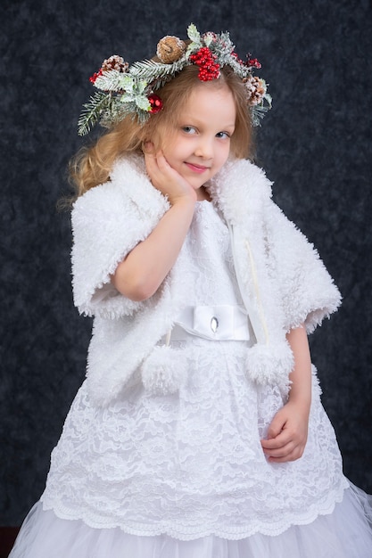 Foto menina linda em um vestido branco com uma guirlanda de natal na cabeça. criança de natal.