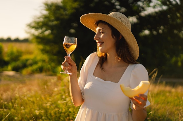 Menina linda em um vestido branco fazendo um piquenique com uma taça de champanhe ou vinho branco