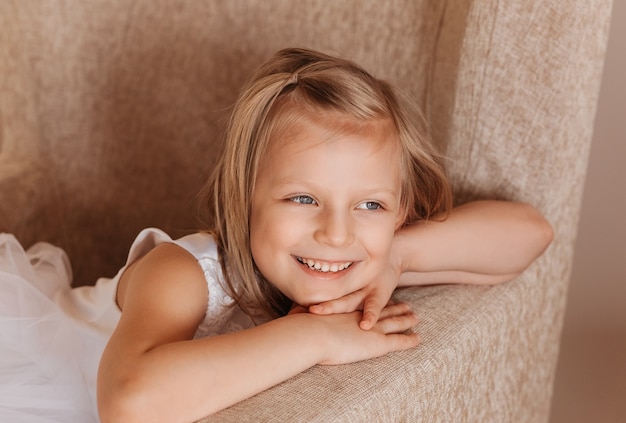 Menina linda em um vestido branco posa para a câmera na cadeira