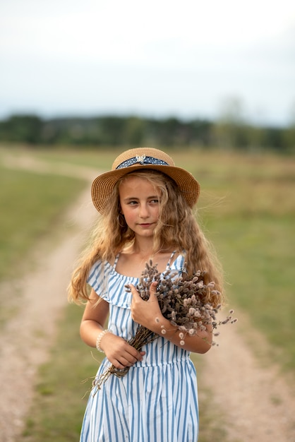 Menina linda em um vestido com cabelos loiros e um chapéu atravessa o Prado