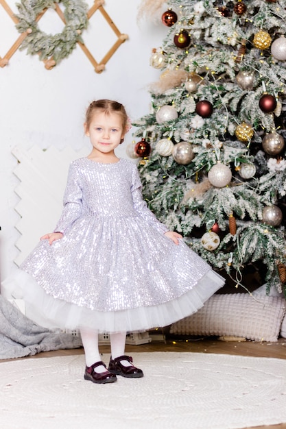 Menina linda em um vestido elegante fica perto da árvore de Natal