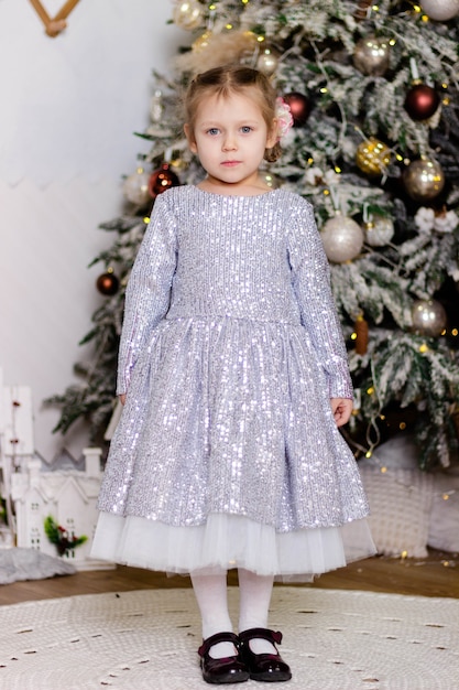 Menina linda em um vestido elegante fica perto da árvore de Natal