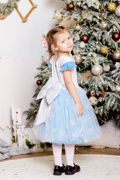 Menina linda em um vestido elegante fica perto da árvore de natal