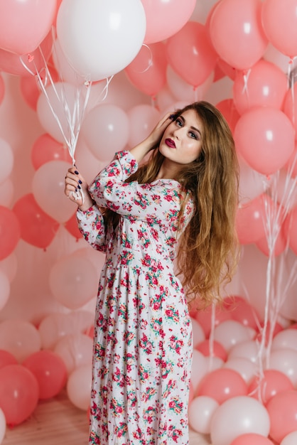 Menina linda em um vestido entre muitas bolas cor de rosa.