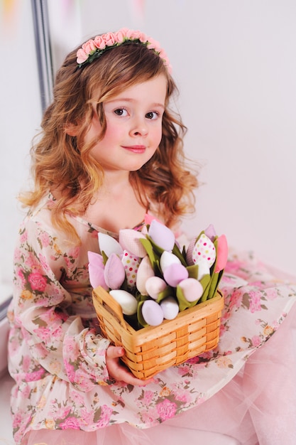 Menina linda em um vestido inteligente senta-se em um peitoril da janela com um buquê de flores tulipas em uma superfície de janela.