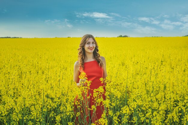 Menina linda em um vestido vermelho fechar no meio do campo amarelo com as flores de rabanete. temporada de primavera